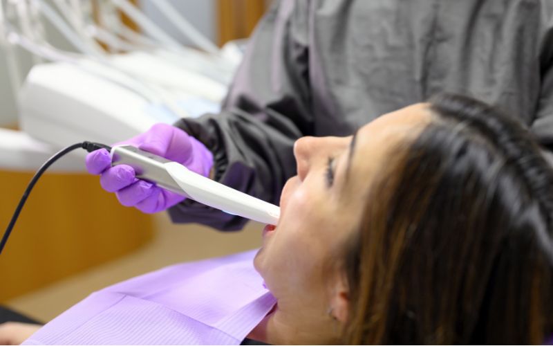 A woman is getting her teeth cleaned in a dentist's office using an intra-oral camera.