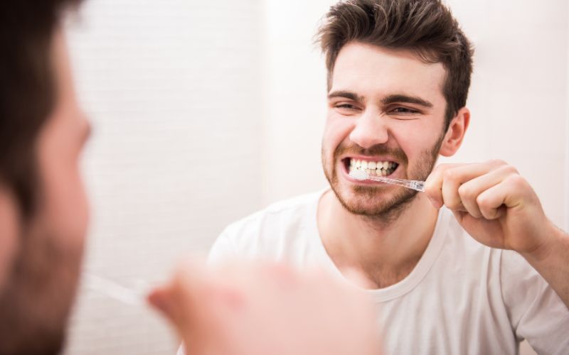 A man making toothbrushing mistakes in front of a mirror.