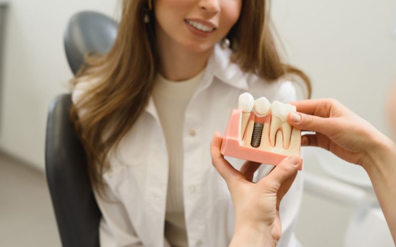 A dentist is demonstrating a dental implant model to a patient.