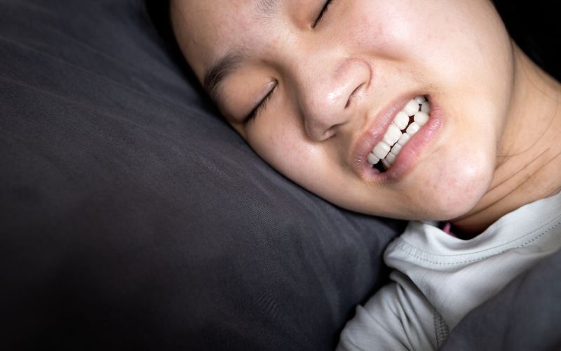 A young Asian woman experiencing teeth grinding while sleeping in bed.
