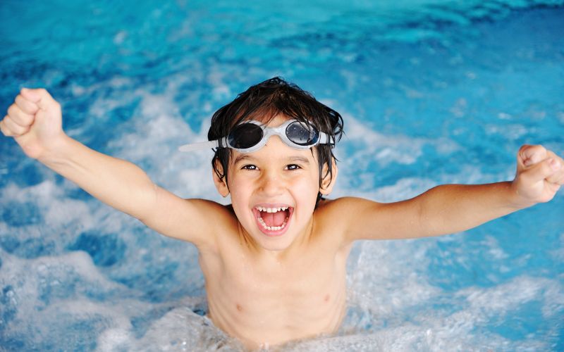 A young boy wearing goggles in a swimming pool, ensuring tooth safety.