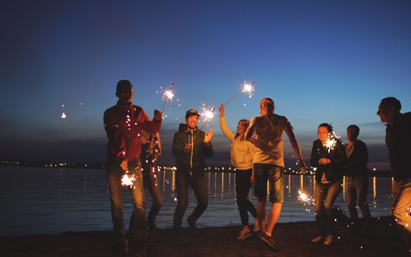 Things to do this long weekend: A group of friends holding sparklers on the beach.