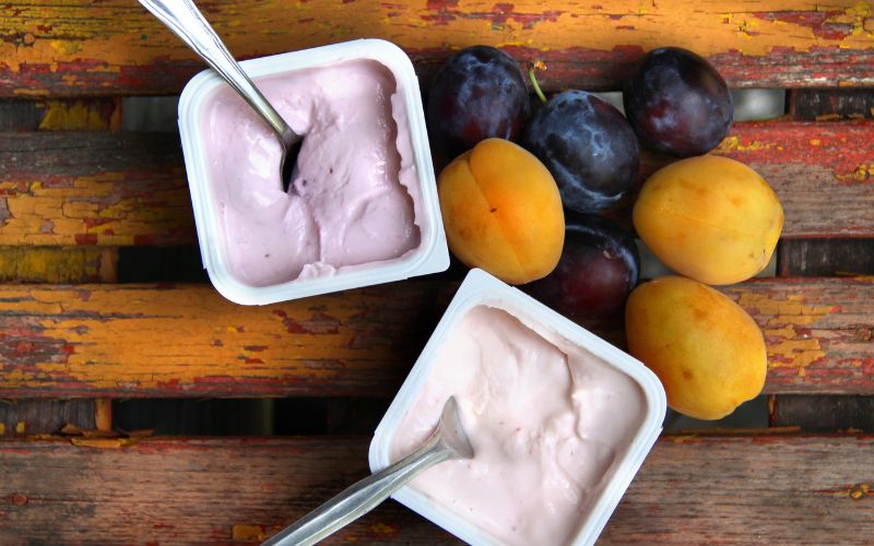 A bowl of yogurt and a bowl of plums on a table.
