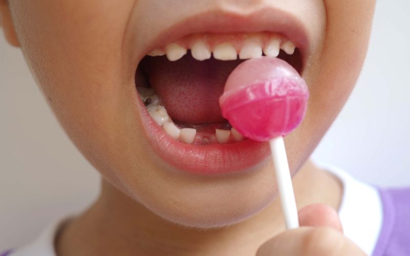 Kid consuming sweet candy lollipop with sugar added, causing loss teeth