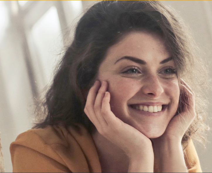 Young woman smiling at results of cosmetic dentistry in mirror in emergency dental in hamilton