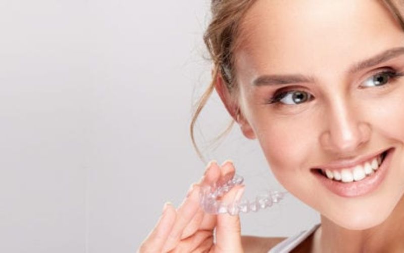 stylist woman smiling with her bright teeth while holding her invisalign hamilton