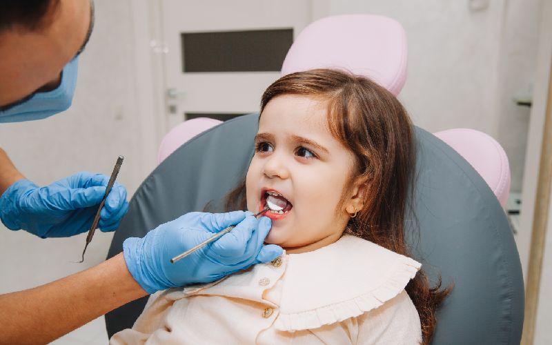 A young girl is getting her tongue tie checked by a dentist.