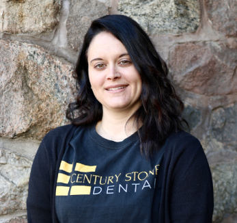 A woman standing in front of a stone wall wearing a t - shirt that says century stone dental.