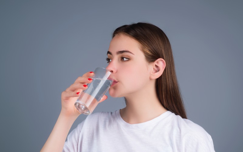 A young woman drinking water from a glass.
