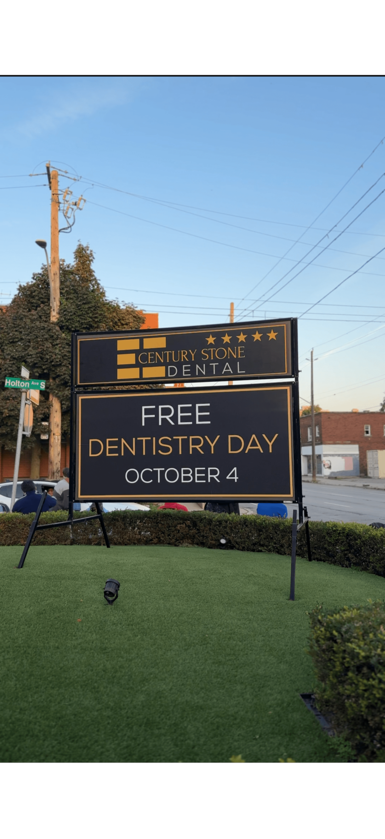 A sign for Century Stone Dental advertising "Free Dentistry Day October 4" is displayed on a lawn near a street corner.