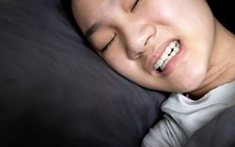 A young Asian woman experiencing teeth grinding while sleeping in bed.