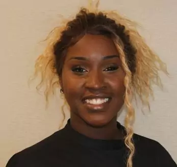 A woman with long hair smiling in front of a wall.