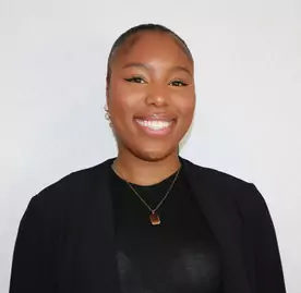A black woman smiling in front of a white wall.