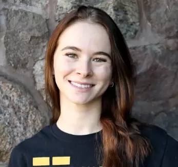 A young woman smiling in front of a stone wall.