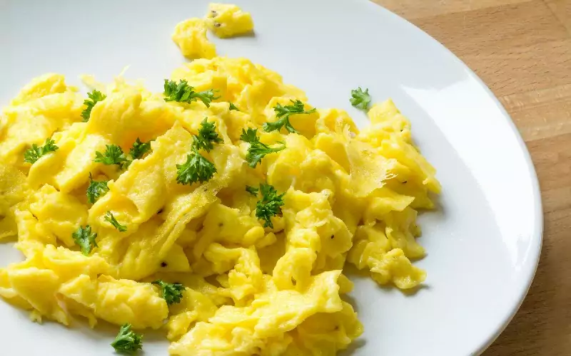 Scrambled eggs on a white plate with parsley.